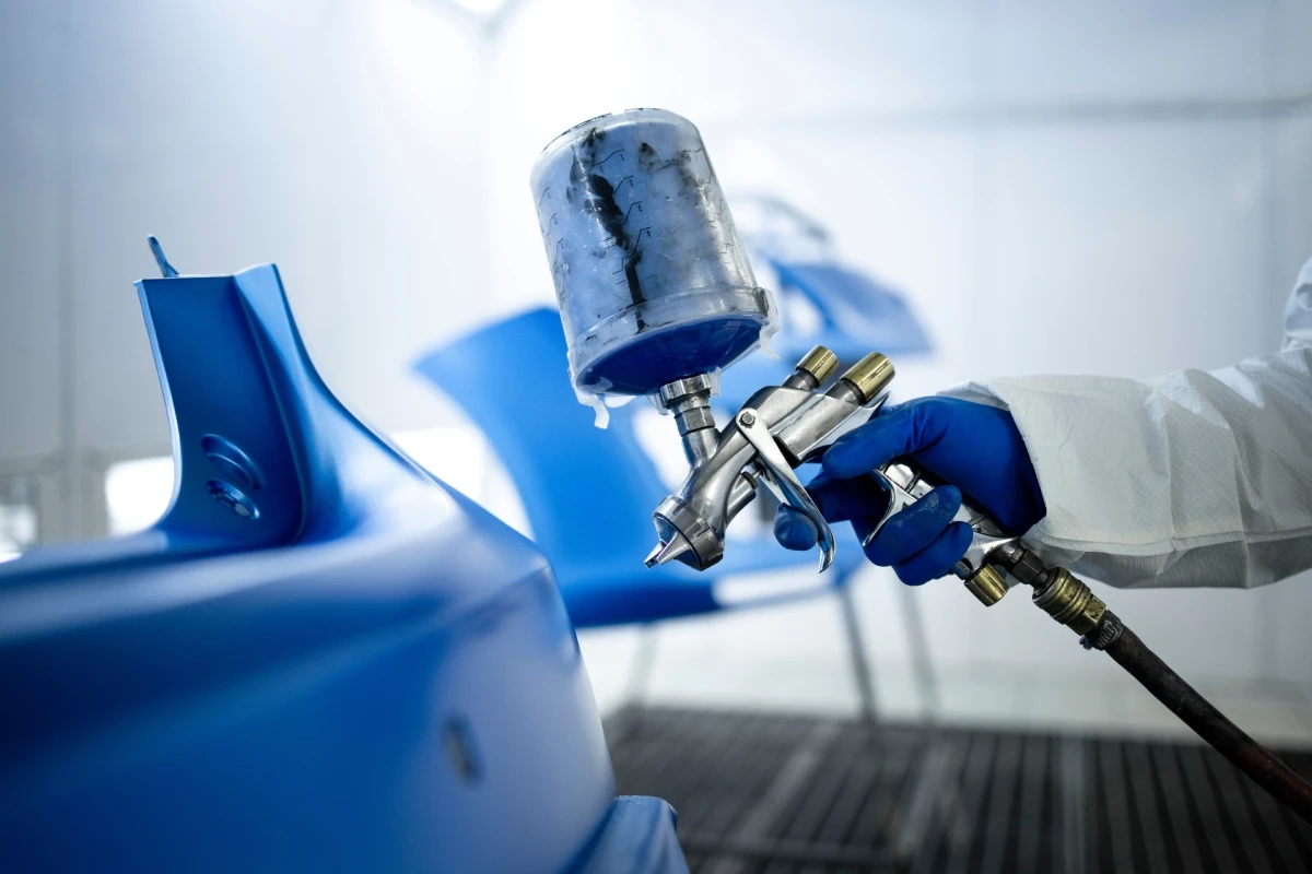 Peça automotiva recebendo pintura azul em cabine de pintura