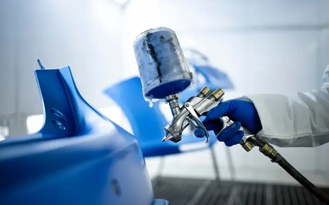 Peça automotiva recebendo pintura azul em cabine de pintura
